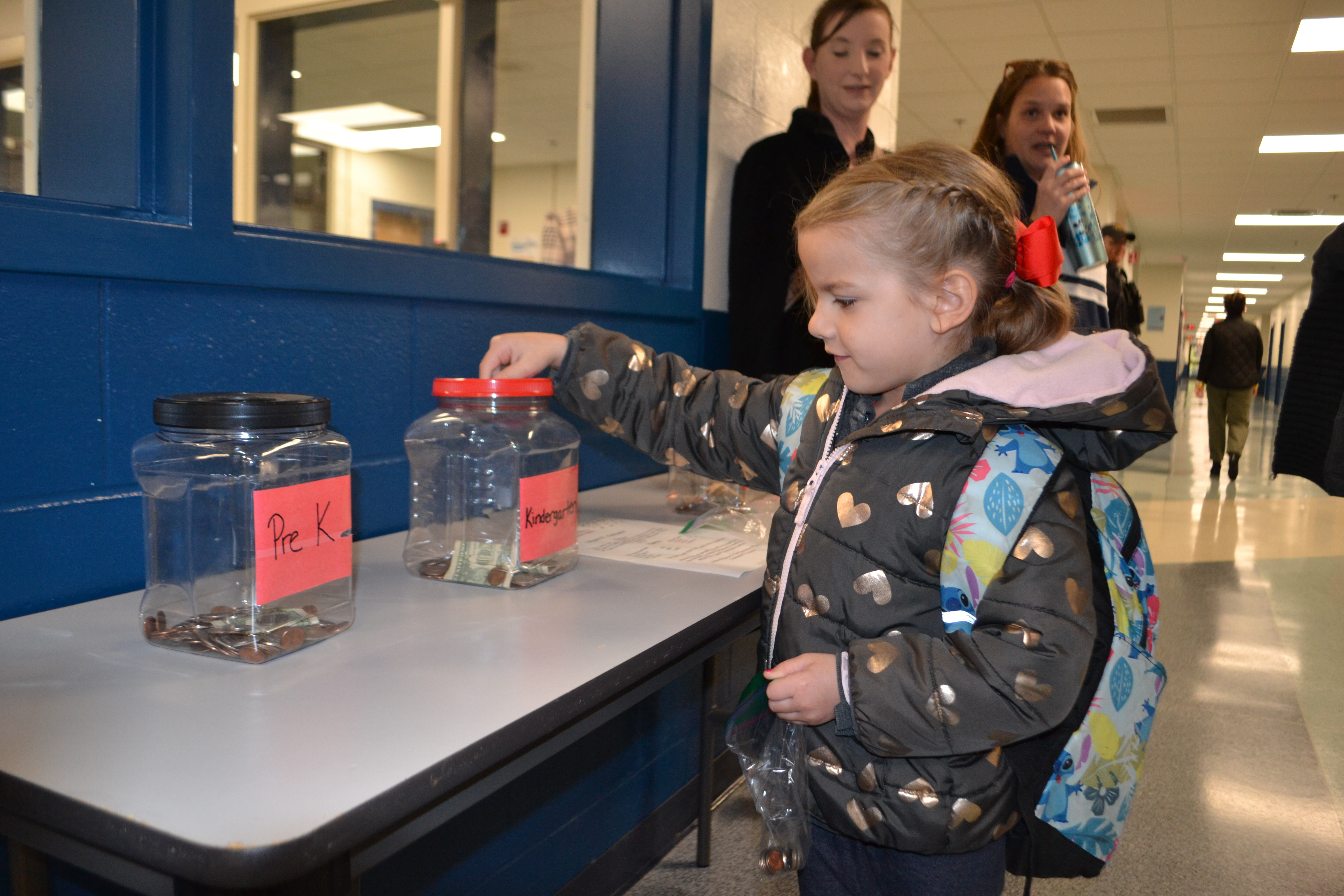 A students places money in a jar for the coin wars competition