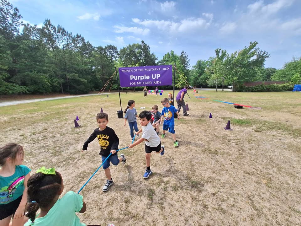 Children work together to pull a wagon full of stuffed animals through a purple Month of the Military Child Banner