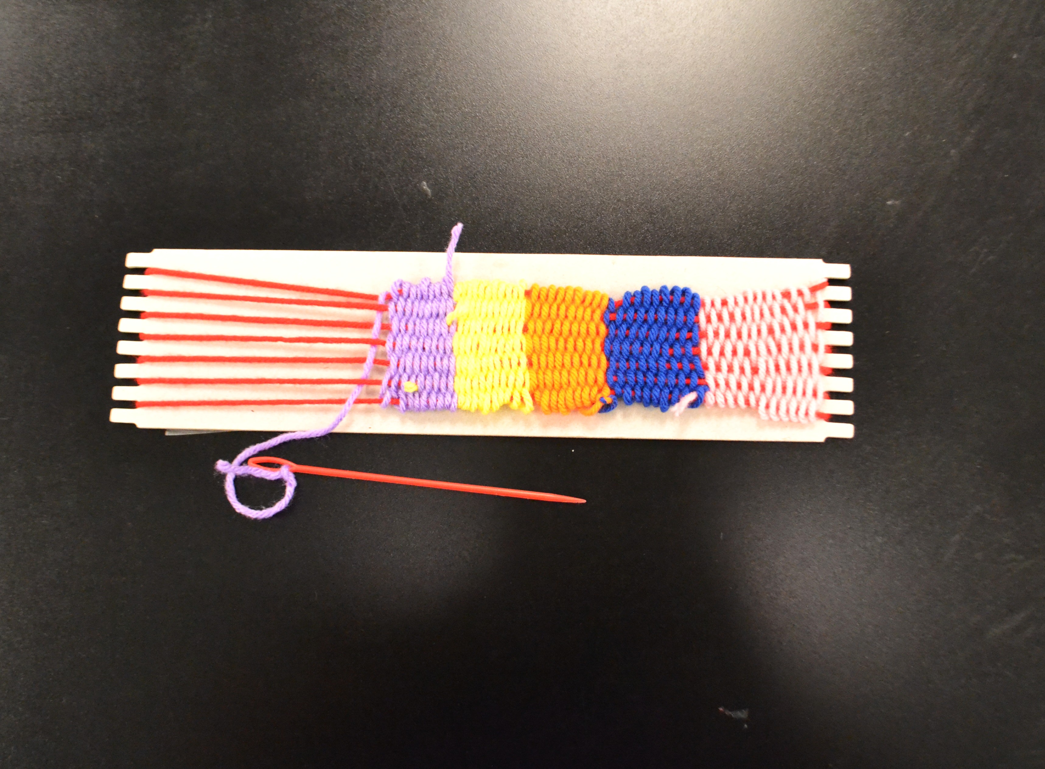 A multicolored weaving project using acrylic yarn still attached to the loom